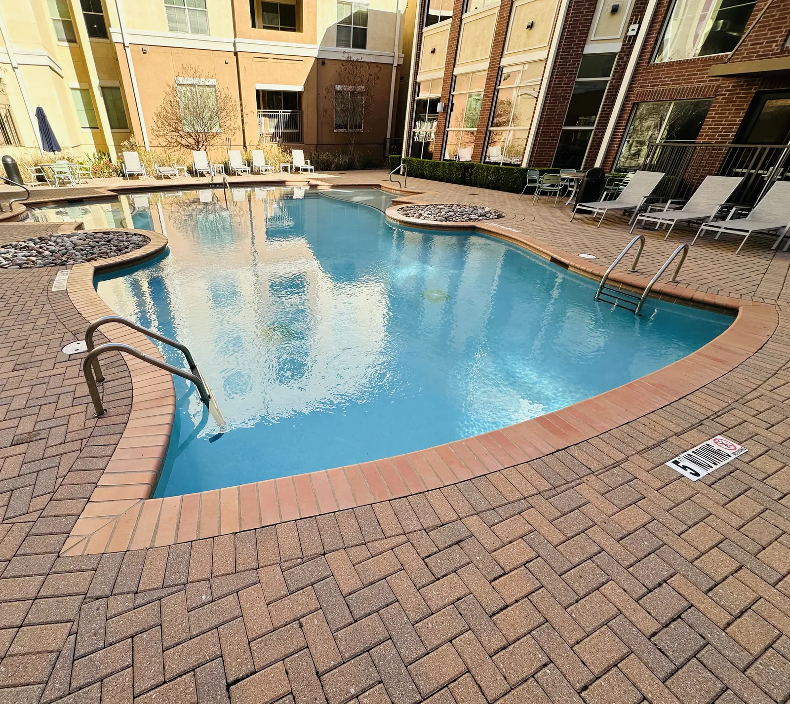 Courtyard apartment pool with brick herringbone pavers and rock planters