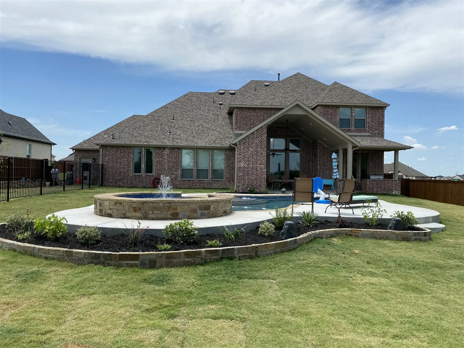 Freeform pool with a raised stone spa and fountain in front of a brick house