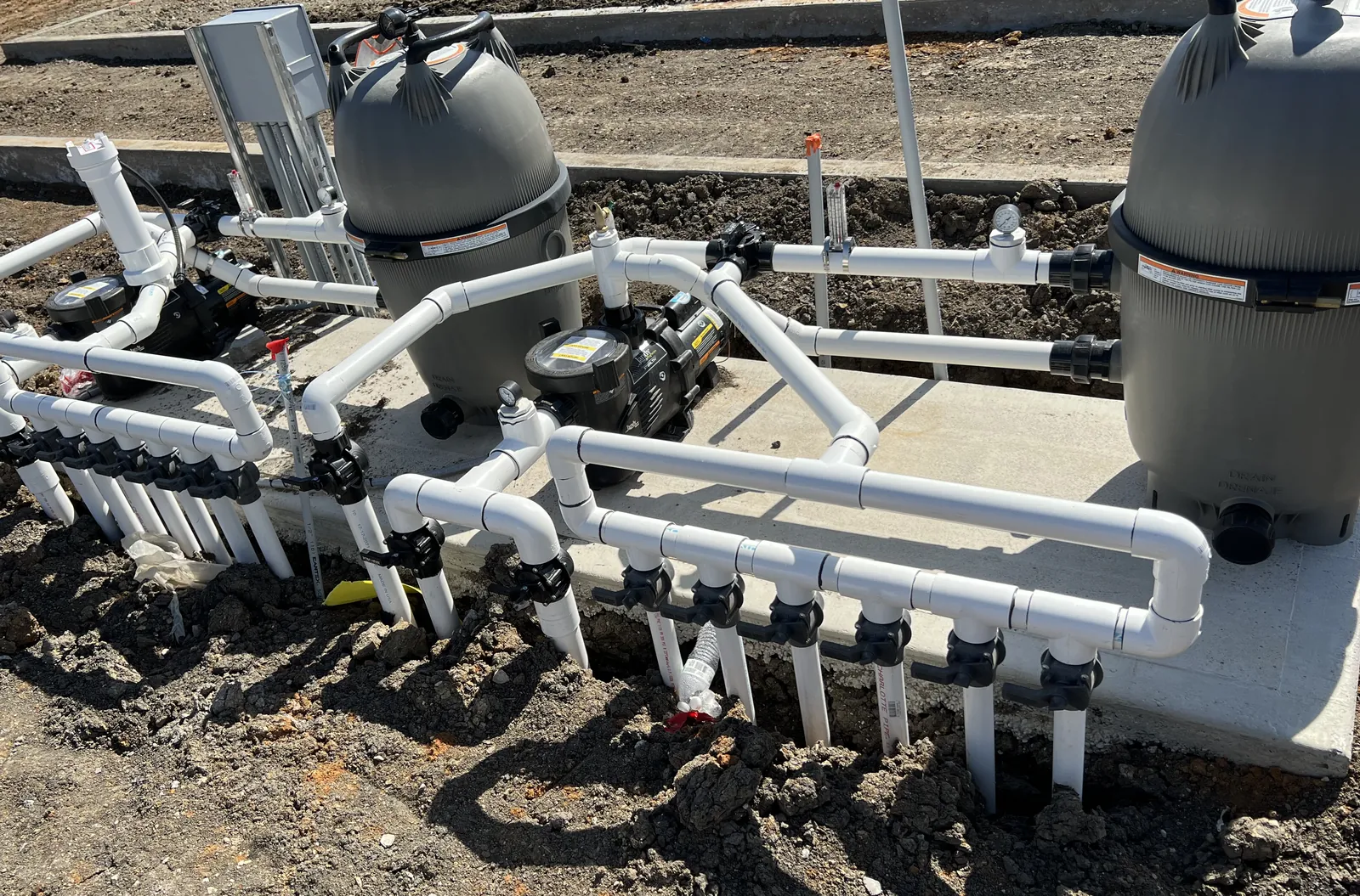 Close-up of two large cartridge filters, pumps, and a valve manifold on the equipment pad for the Hollyhock center fountain in Frisco, TX
