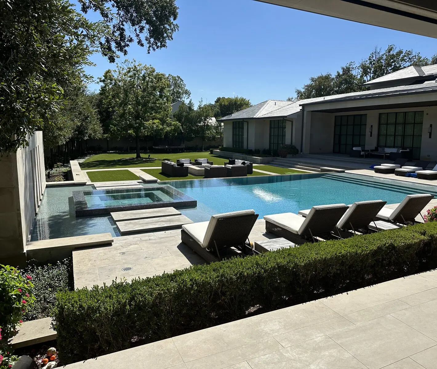 Pool and raised spa with stepping pads, a hedge, and lounge chairs