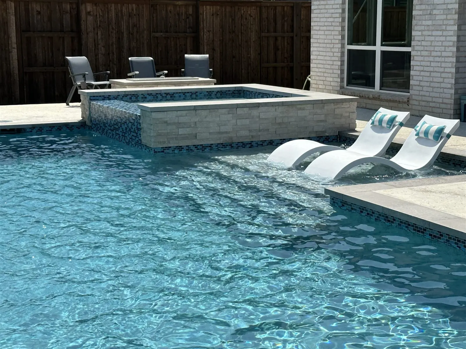 In-pool tanning ledge with two white loungers beside a raised stone spa
