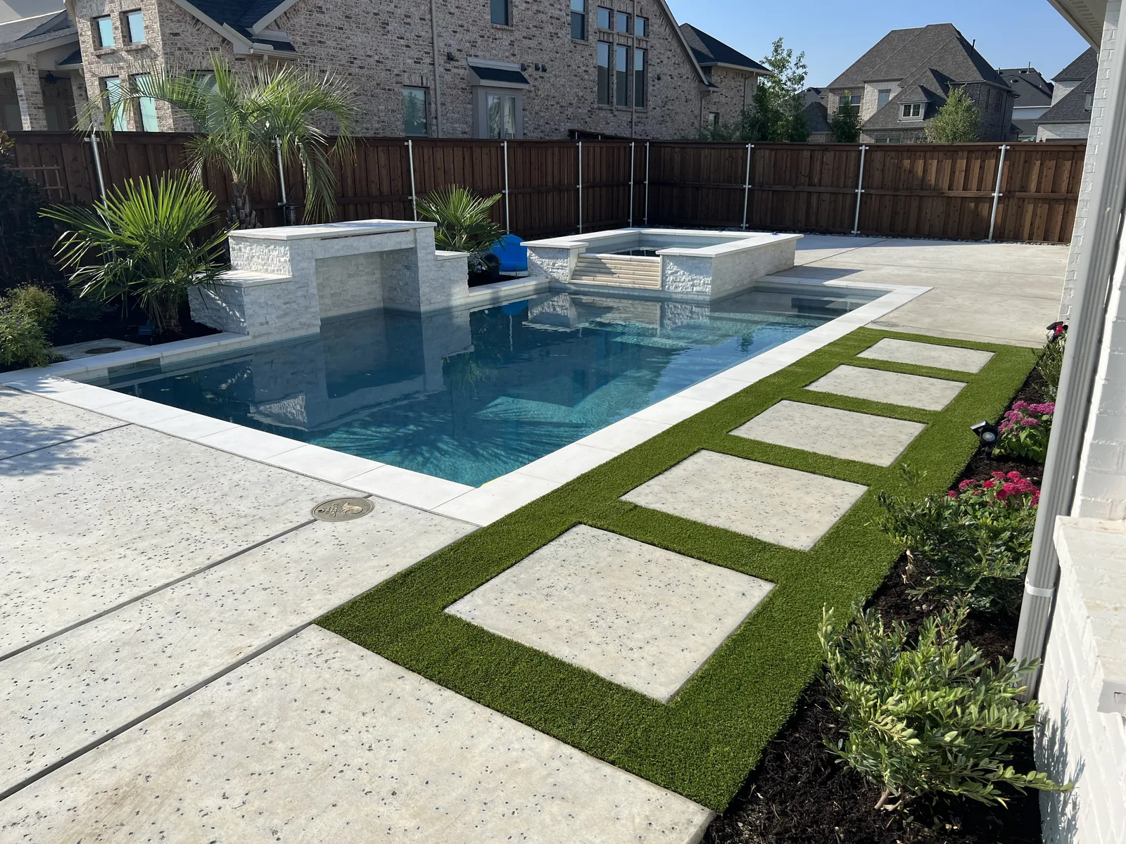 Rectangle pool with a raised stone spa, a spillway wall, and turf stepping pads